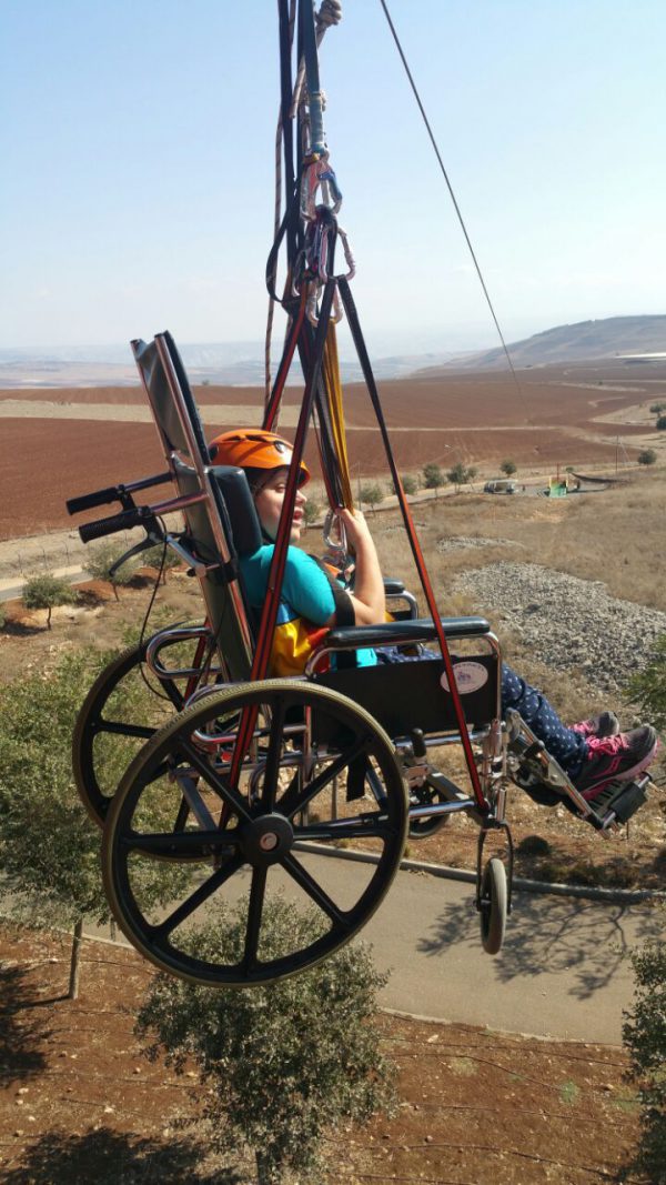 ילדה יושבת בכיסא גלגלים מתחיל ירידה באומגה, על רקע השדות.